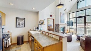 Una cocina moderna con una isla central, un comedor con chimenea y ventanas amplias con vistas.