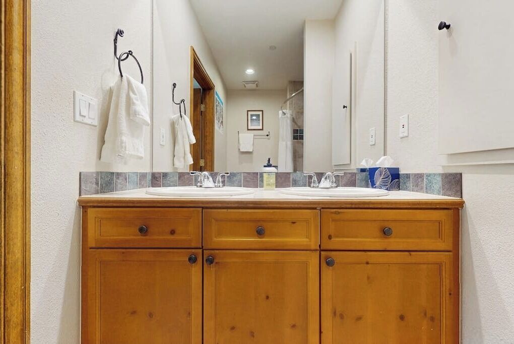 A bathroom with a wooden vanity, two sinks, and a mirror.