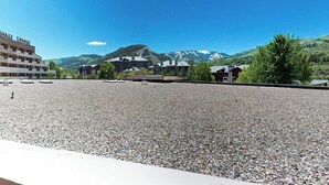 Un hotel con un patio de grava, edificios de varios pisos y un paisaje montañoso de fondo.