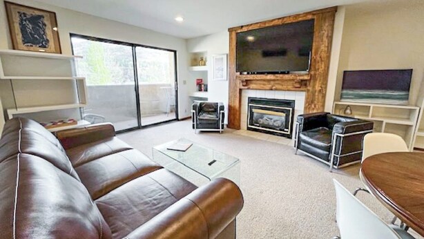 Una sala de estar moderna con un sofá de cuero, una mesa de centro de vidrio, una chimenea, un televisor de pantalla plana y un comedor.
