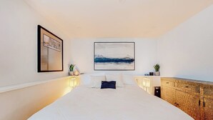Een groot bed met een gewatteerde spreidek, een aan de muur hangend schilderij, bedlampjes en een gestructureerde kast.