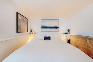 Ein großes Bett mit einer gesteppten Decke, ein Wandbild, Nachttischlampen und ein Cabinet mit Struktur.