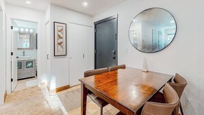 Een eethoek met een houten tafel en stoelen, een donkere deur, een lijstwerk kunstwerk en een ronde spiegel aan de muur.