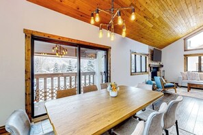 Ein Essbereich mit Holztisch, Stühlen, einer Chandelierleuchtre und Blick durch große Fenster.