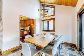 Ein Essbereich mit Holztisch und Stühlen, einer Kristallleuchter und einer Küche im Hintergrund.
