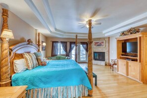 Une chambre spacieuse avec un grand lit, un ventilateur de plafond, une télévision et une cheminée.