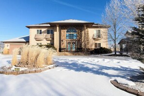 A two-story house with a stone facade, a front porch, and a snow-covered driveway.