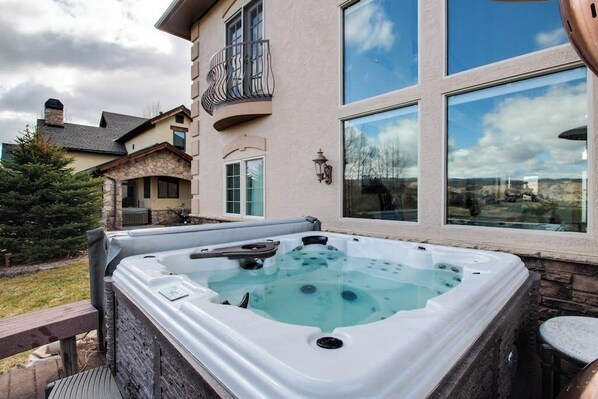 A hot tub outside a house with a balcony, large windows, and a stone facade.