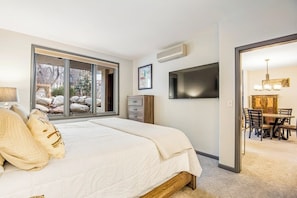 Ein Schlafzimmer mit einem großen Bett, einem Fernseher, einem Fenster mit Blick auf Felsen und einem Essbereich, der durch eine offene Tür sichtbar ist.