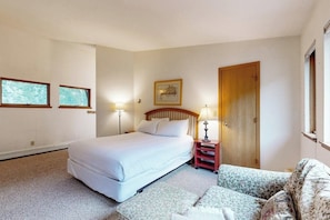 Ein Schlafzimmer mit Bett, Nachttischen, einer Tür und zwei Fenstern.