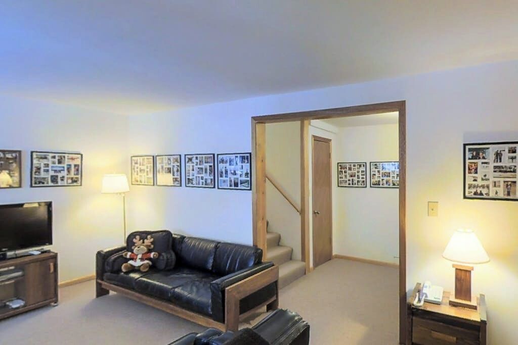 A living room with a television, a leather sofa, a lamp, and framed pictures on the wall.
