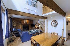 Ein Wohnzimmer mit Kamin, einer Couch, einem Esstisch und einer Treppe.