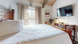 Una camera da letto con un letto grande, una scrivania in legno, una TV a schermo piatto, una ventola e una finestra con tende.