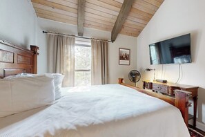 A bedroom with a large bed, a wooden desk, a flat-screen TV, a fan, and a window with curtains. - Newly Renovated Condo - on the Bus Line (Vail)