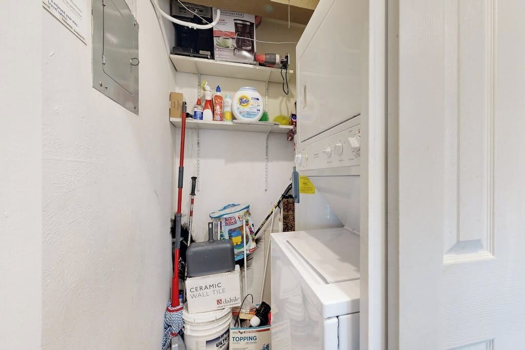 A narrow bathroom with a white wall, a shelf with cleaning supplies, a bucket labeled 'CERAMIC WALL TILE,' and a white washing machine.