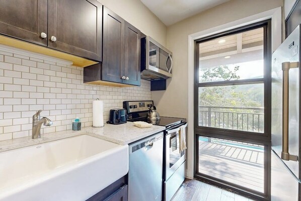A kitchen with a dishwasher, oven, microwave, and a large window with a view of a deck. - Newly Renovated Condo - on the Bus Line (Vail)