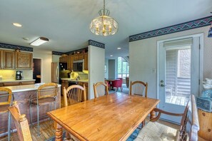 A dining area with a wooden table and chairs, a chandelier, and a kitchen in the background. - Secluded valley home w/ private balcony, grill, shared tennis - close to trails (East Vail)