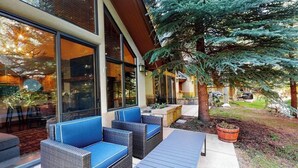 Une terrasse avec des meubles en osier et une table, un grand arbre et un bâtiment doté de grandes fenêtres.