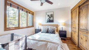 Une chambre à coucher comprenant un lit, des tables de chevet, un ventilateur de plafond, une grande fenêtre et une armoire en bois.