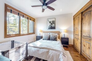 Ein Schlafzimmer mit einem Bett, Nachttischen, einem Deckenventilator, einem großen Fenster und einem Holzschrank.