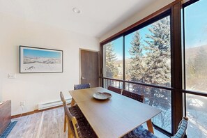 Ein Essbereich mit Holztisch und Stühlen, einem gerahmten Bild an der Wand und einem großen Fenster mit Blick auf Bäume.