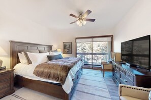Ein Schlafzimmer mit Bett, Deckenventilator, Fernseher, Kommode und Fenster mit Blick.