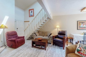 Ein Wohnzimmer mit einer Couch, zwei Sesseln, einem Couchtisch, einer Lampe, einer Treppe und einem Bild an der Wand.