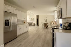 A modern kitchen with white cabinetry, a stainless steel refrigerator, and a dining area with a table and chairs. - Harbor Haven #1 (Riverview)