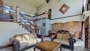 Ein geräumiger Wohnbereich mit Treppe, Ledersofas, einem Holztisch und einer Backsteinwand.