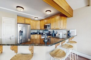 A kitchen with wooden cabinets, a stainless steel refrigerator, a microwave, a stove, and a bar area with stools. - Spacious mountain retreat minutes from Beavercreek w/shared pool/hot tub & patio (Edwards)