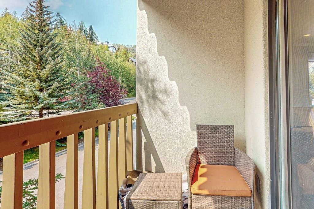 Un balcon doté de meubles en osier, d’une balustrade en bois et offrant une vue sur les arbres.