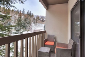 Ein Balkon mit Korbmöbeln, einer Glastür und Blick auf schneebedeckte Bäume und Gebäude.
