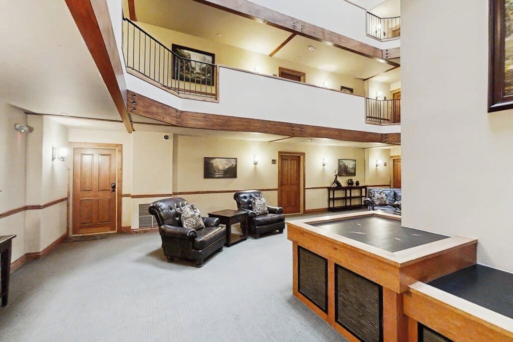 A spacious indoor area with a pool table, leather chairs, and a staircase leading to an upper level.