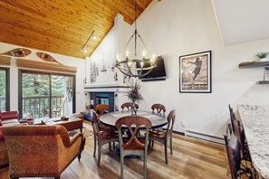 A dining area with a round table and chairs, a chandelier, and a television mounted on the wall. - Spacious condo w/ full kitchen, shared hot tub & perfect location (Beaver Creek)