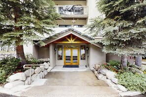 A building with a central entrance, a balcony on the upper floor, and surrounding greenery. - Spacious condo w/ full kitchen, shared hot tub & perfect location (Beaver Creek)