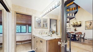Un dormitorio con cama, un baño con tocador y una escalera que lleva a un comedor.