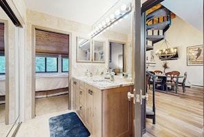 A bedroom with a bed, a bathroom with a vanity, and a staircase leading to a dining area. - Spacious condo w/ full kitchen, shared hot tub & perfect location (Beaver Creek)