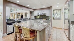 Une cuisine spacieuse dotée d’un grand îlot central, de meubles blancs et offrant une vue sur l’extérieur.