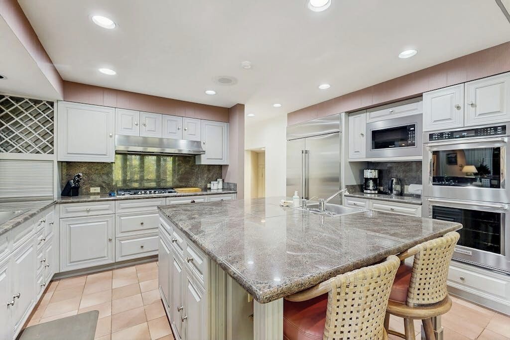 A modern kitchen with stainless steel appliances, white cabinetry, and a central island with bar stools.