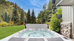 Un bain à remous dans un jardin, avec un mur en pierre, une antenne parabolique et une chaîne de montagnes en arrière-plan.