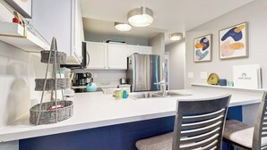 A modern kitchen with white cabinets, a stainless steel refrigerator, a sink, and a bar area with two chairs. - Mountain-view condo with outdoor pool, fireplace, patio, pool table & W/D (Edwards)