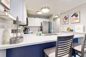 A modern kitchen with white cabinets, a stainless steel refrigerator, a sink, and a bar area with two chairs. - Mountain-view condo with outdoor pool, fireplace, patio, pool table & W/D (Edwards)