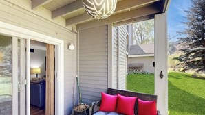 A covered porch with a sofa, a glass table, and a potted plant. - Mountain-view condo with outdoor pool, fireplace, patio, pool table & W/D (Edwards)