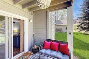 A covered porch with a sofa, a glass table, and a potted plant. - Mountain-view condo with outdoor pool, fireplace, patio, pool table & W/D (Edwards)