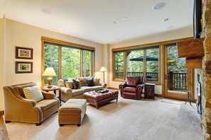 A spacious living room with large windows, a fireplace, and a stone wall. - Second-floor retreat near the slopes with grill, fireplace, pool, & hot tub (Edwards)