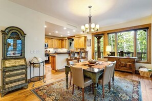 A spacious kitchen with wooden cabinets, a dining area with a table and chairs, and large windows offering a view of trees. - Second-floor retreat near the slopes with grill, fireplace, pool, & hot tub (Edwards)