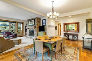 A spacious living room with a fireplace, a dining area with a table set for four, and a large window offering a view of the outdoors. - Second-floor retreat near the slopes with grill, fireplace, pool, & hot tub (Edwards)