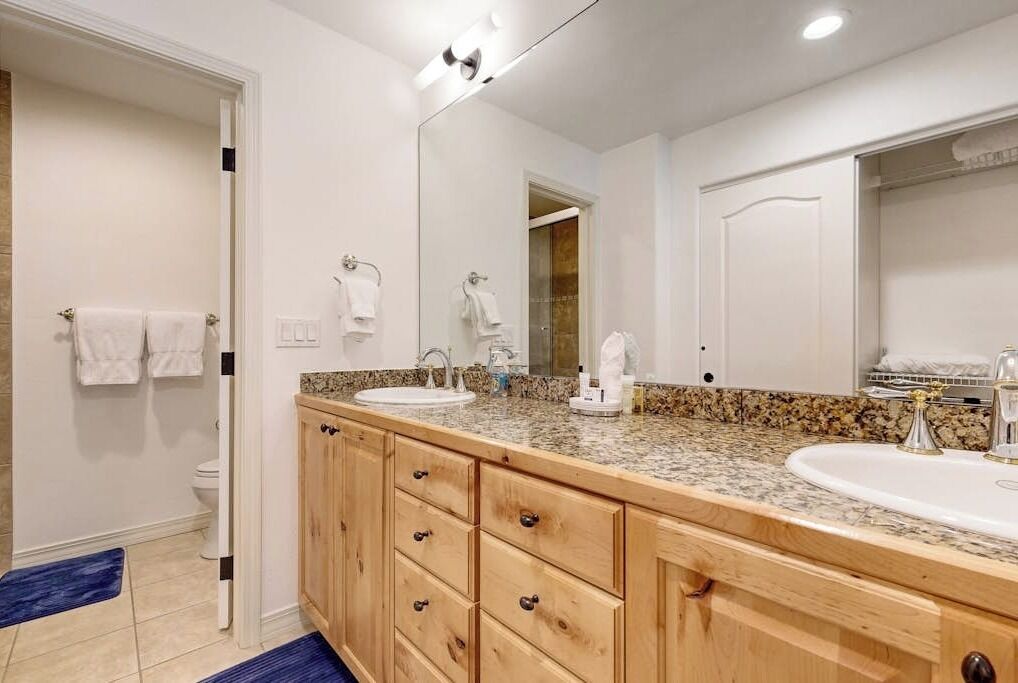 A bathroom with a double sink, wooden cabinets, a large mirror, and a toilet.