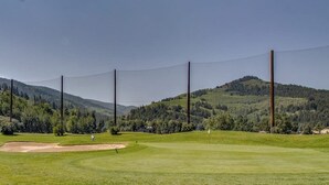 Ein Golfplatz mit blauem Himmel, einer Fahne und einem entfernten Berg.