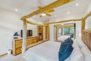 Ein Schlafzimmer mit Holzboden, einem Bett mit Kissen, einem Schminktisch, einem Fernseher und einem Spiegel.